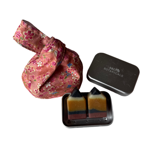 Small tin with three soap bars and a handmade floral fabric pouch on a white background